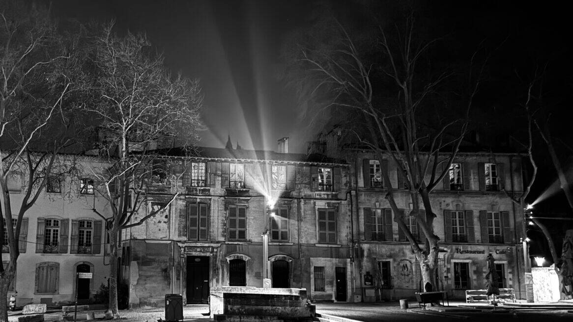 Place du Palais des Papes d'Avignon la nuit, halo lumineux depuis les mats, réglages nocturnes par L'Acte Lumière.