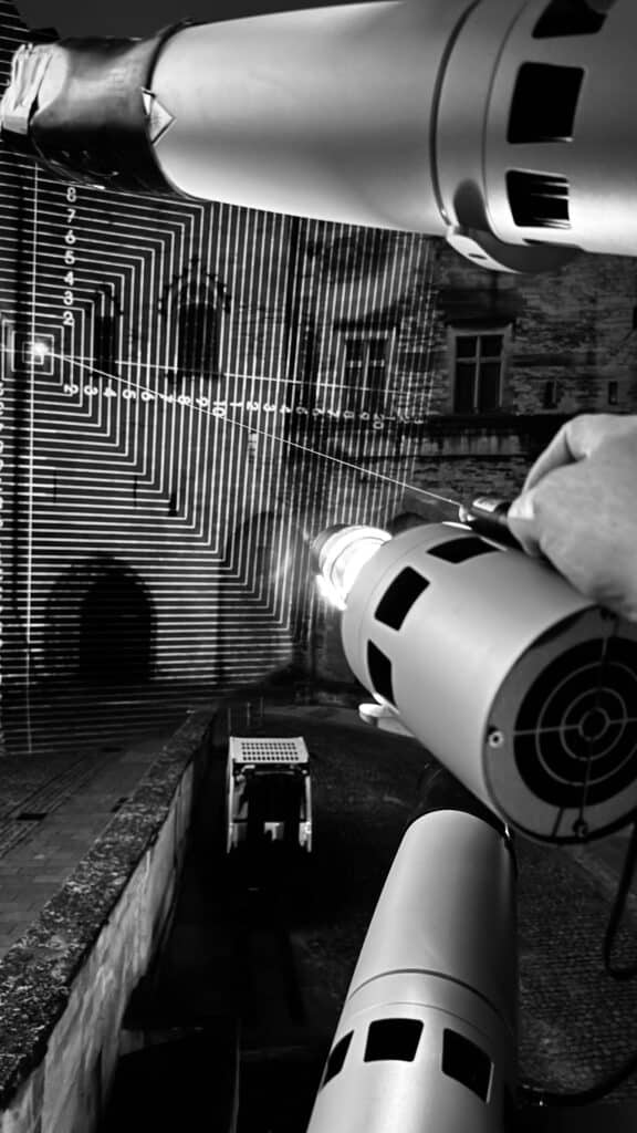 Main réglant un projecteur lors des essais nocturnes au Palais des Papes d'Avignon, tir laser de visée et mire.