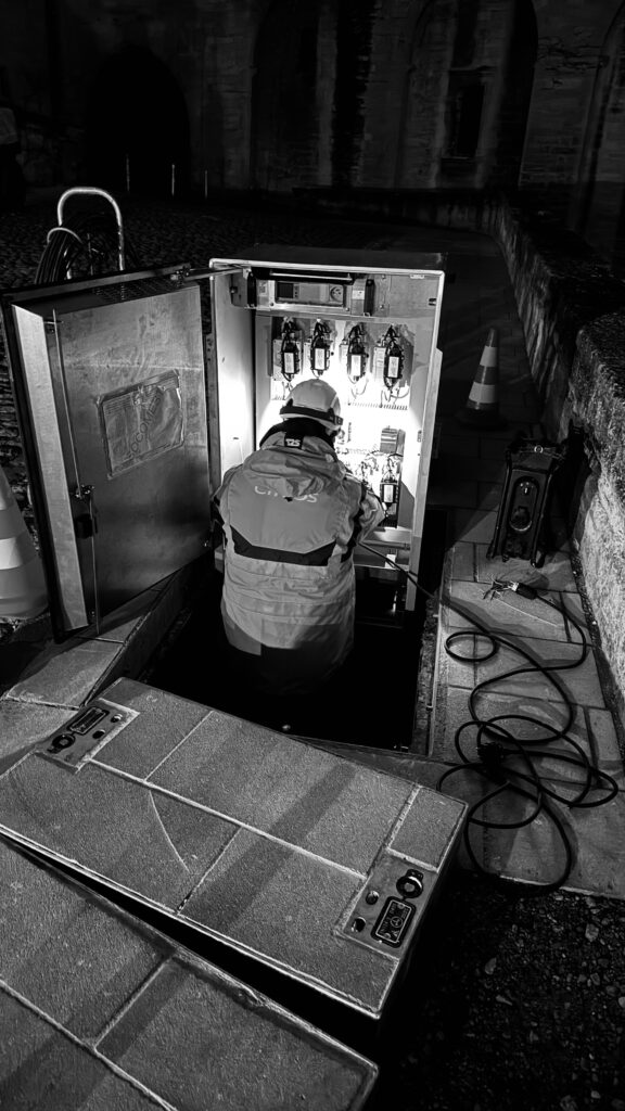 Électricien sur tableau de distribution enterré d'alimentation du Palais des Papes, chantier de nuit.
