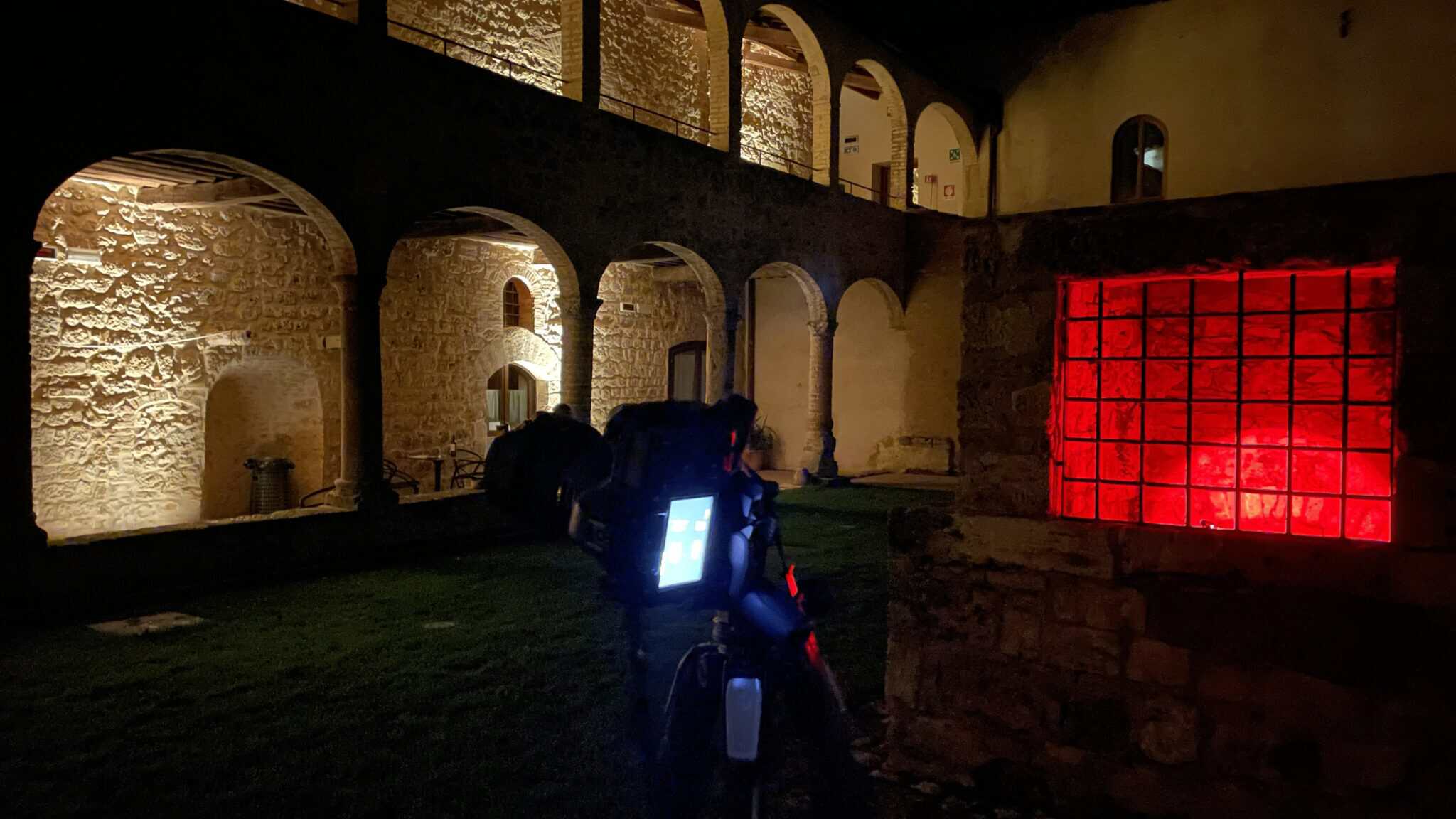 Le cloître d'Abbadia a Isola de nuit, arcades éclairées en lumière chaude, panneau rouge, Going Dark 2024